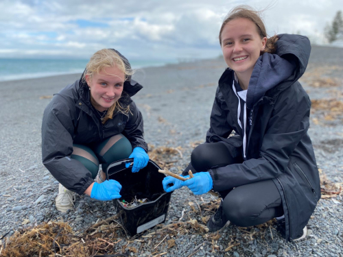 Two young people on a beach with a bucket of plastic they have cleaned up